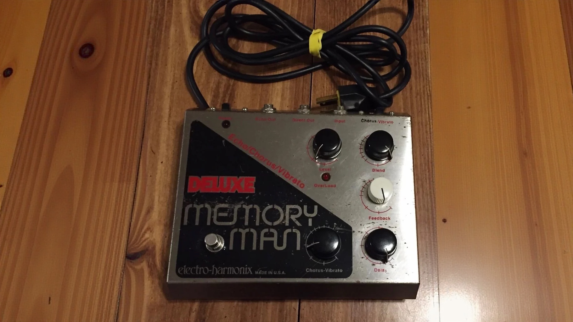 First generation Electro-Harmonix Deluxe Memory Man, worn silver and black enclosure with red lettering, connected mains cable coiled above.