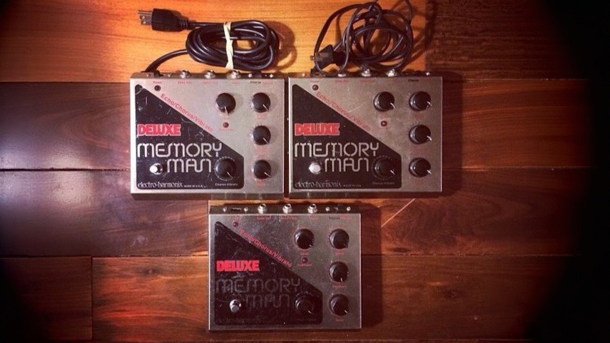 Three generations of Electro-Harmonix Deluxe Memory Man pedals laid out on a wooden surface.